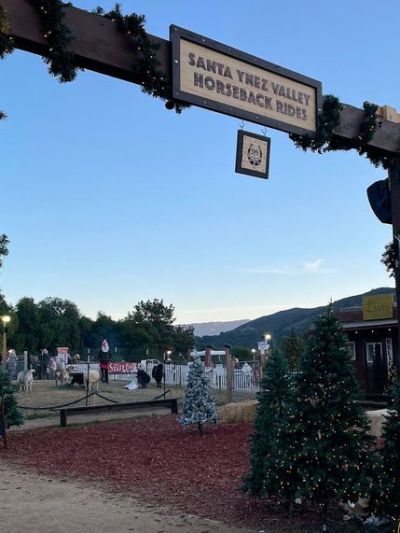 Decorated wooden archway reads 'Santa Ynez Valley Horseback Rides' with trees and hills in the background.